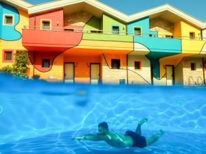 a man swimming in a swimming pool in front of a building at Alexandra Golden Boutique Hotel-Adults Only in Chrysi Ammoudia