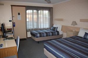 a hotel room with two beds and a desk at Raglan Motor Inn in Warrnambool