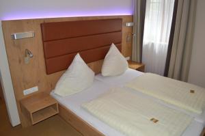 a bed with a wooden headboard and white pillows at Hotel Daimerwirt in Moosinning