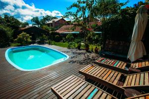 una piscina en una terraza con banco y sombrilla en Pousada Rosa da Praia, en Praia do Rosa