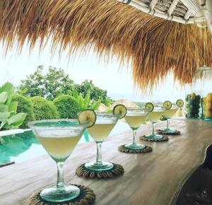 a row of cocktails on a table under a straw umbrella at Gravity Eco Boutique Hotel - Adults Only in Uluwatu