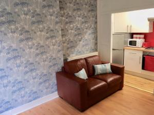 a brown leather couch in a living room with a kitchen at Watson Crescent in Edinburgh