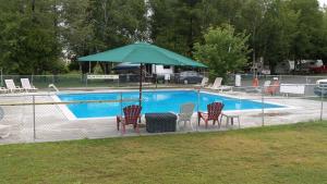 a pool with a green umbrella and chairs and a table with a grill at Franklin Motel, Tent & Trailer Park in North Bay