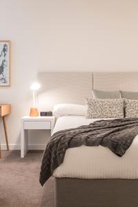 a white bedroom with a bed and a night stand at Caroline Serviced Apartments Sandringham in Sandringham