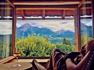 una persona sentada en una silla mirando por la ventana con una copa de vino en Chambre d'Hôtes La Grange des Ecrins en Chabottes