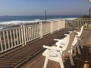 two white chairs sitting on a deck near the beach at Fairlight Beach House in Umdloti