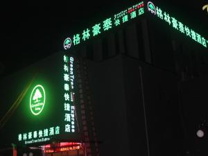 GreenTree Inn Tianjin Xiqing District Xiuchuan Road Sunshine 100 في تيانجين: مبنى عليه لافتات نيون في الليل
