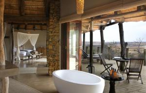 a bathroom with a bath tub and a bedroom at Nambiti Plains Lodge in Nambiti Game Reserve