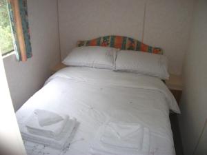 a bed in a small room with white sheets and pillows at caravan nestled away amongst trees on edge of farm yard in Bala