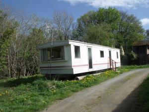 a white trailer sitting on the side of a road at caravan nestled away amongst trees on edge of farm yard in Bala