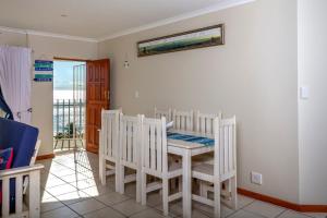 a dining room with a table and chairs and a balcony at The White House Apartment in Mossel Bay