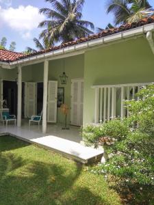 a green house with a porch and a palm tree at Bungalow Sud in Habaraduwa Central