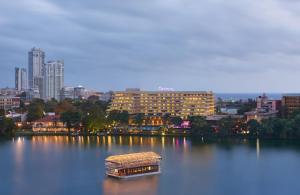 un bateau dans un lac avec une ville en arrière-plan dans l'établissement Cinnamon Lakeside, à Colombo