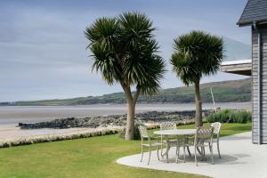 a table and chairs with palm trees and the ocean at Airds Bay Luxury Beach House in Gatehouse of Fleet