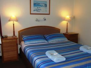 a bed with blue and white striped sheets and two lamps at Aquarius Motel in Belmont