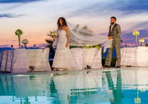 Os noivos estão ao lado de uma piscina. em Marini Luxury Apartments and Suites em Egina