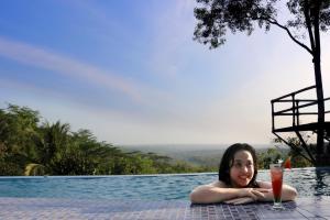 une femme qui se couche dans une piscine avec une boisson dans l'établissement Rajaklana Resort and Spa, à Bantul