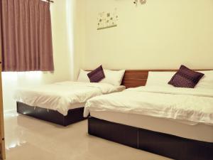 a bedroom with two beds with white sheets and purple pillows at Lu He Feng Homestay in Luodong