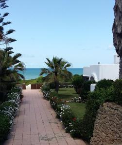 a walkway with flowers and palm trees and the ocean at Villa meublée face à la mer, Golf et Verdure in El Jadida