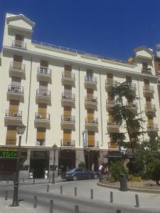馬德里的住宿－特里亞納旅館，一座白色的大建筑,前面有汽车停放