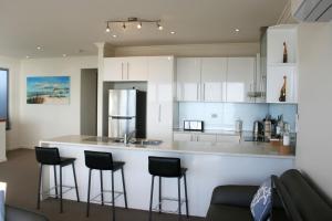 une cuisine avec des placards blancs et un bar avec des tabourets dans l'établissement Penneshaw Oceanview Apartments, à Penneshaw