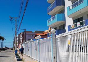 two people walking down a sidewalk next to a white fence at Rental Home Caminho do Mar Prainha in Arraial do Cabo