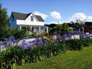 a white house with a white fence and purple flowers at Ashley Villa BnB in Takaka