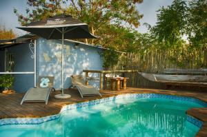 a swimming pool with an umbrella and chairs and a table at The Old House in Kasane