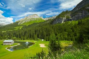 a golf course in the mountains next to a river at Hotel Gotthard in Lech am Arlberg