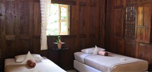 two beds in a room with wooden walls and a window at Puri Brata in Parangtritis