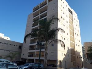 um edifício branco alto com uma palmeira em frente em Shoam street apartment sea view Ashdod em Ashdod