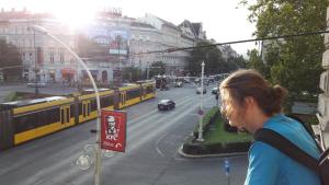 Una donna che guarda in una strada di città con un treno di Pal's Mini Hostel a Budapest