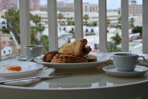 una mesa con un plato de pan y tazas de café en The Best Holiday, en Playa de las Américas