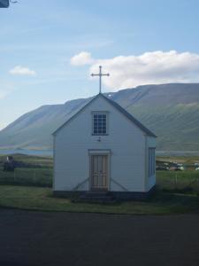 uma pequena igreja branca com uma cruz em cima em Ljósavatn Guesthouse em Kiðagil