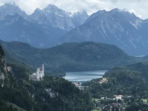 a castle on a hill with a lake and mountains at Landhaus & Pension Christian in Füssen