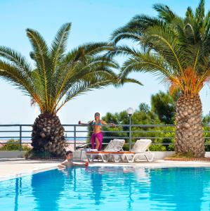a woman standing next to a swimming pool with two palm trees at City's Hill Hotel in Kuşadası