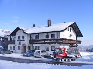 uma casa coberta de neve com um tractor à sua frente em Pension Philippsreut "Zum Pfenniggeiger" em Philippsreut
