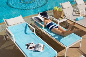 a woman in a hat laying on a beach chair next to a pool at Hôtel Barrière Le Majestic Cannes in Cannes