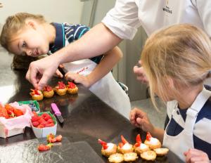 two children in a kitchen preparing strawberries on muffins at Hôtel Barrière Le Majestic Cannes in Cannes