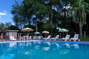 uma piscina com cadeiras, mesas e guarda-sóis em Hotel Jardim Europa em Ijuí