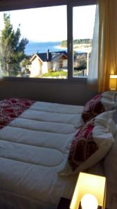 Una cama con sábanas blancas y una ventana en una habitación en Departamento con vista al lago en Bariloche. en San Carlos de Bariloche