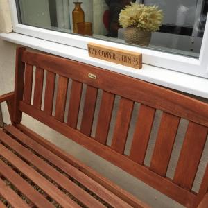 a wooden bench sitting under a window with a sign on it at The Copper Coin in Winford