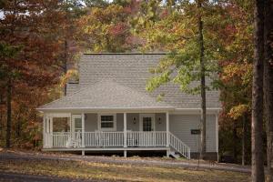 a white house with a porch in the woods at Stonehill Cottages in Mena