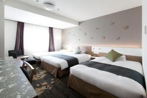 富山市にある富山エクセルホテル東急のベッド3台とテーブルが備わるホテルルームです。