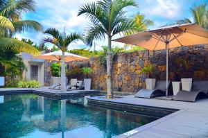 a swimming pool with umbrellas and chairs next to a wall at Paradise Beach Luxury Beachfront Apartment Pointe d'Esny in Pointe d'Esny