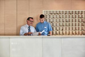 two men standing at a counter looking at a paper at Candia Hotel in Athens