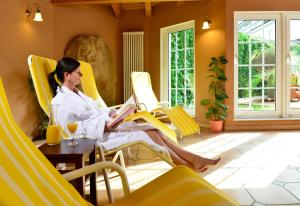 una mujer sentada en una silla amarilla leyendo un libro en Hotel Der Lindenhof, en Gotha