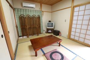 a living room with a table and a tv at Guesthouse Hikari in Kumano