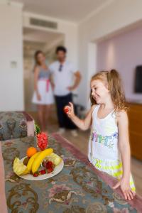 a little girl standing next to a table with a plate of fruit at Side Crown Serenity All Inclusive in Side