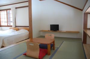 Habitación pequeña con cama, mesa y TV. en Il Bosco, en Hakuba